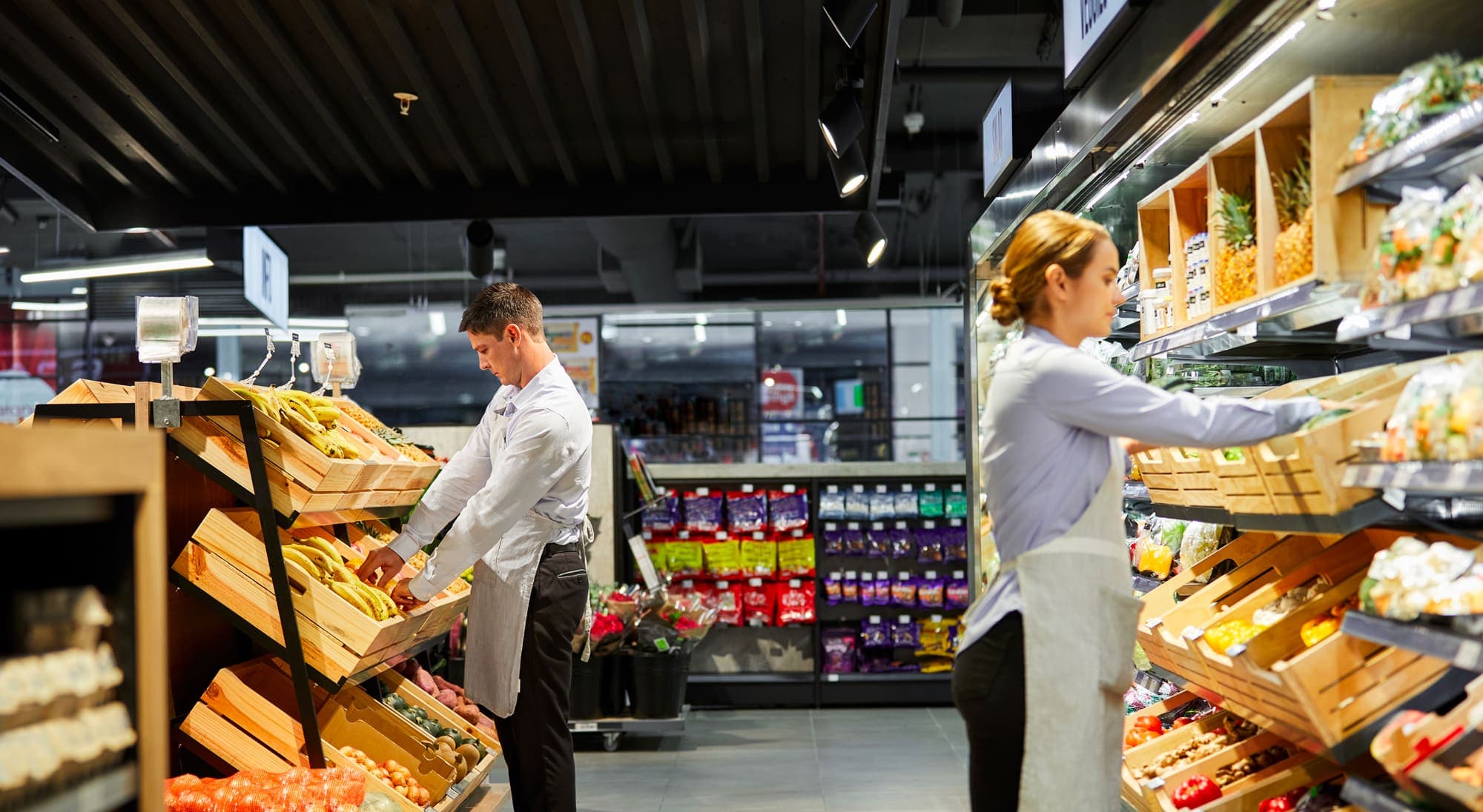 Two supermarket staff stocking fruit and vegetable displays
